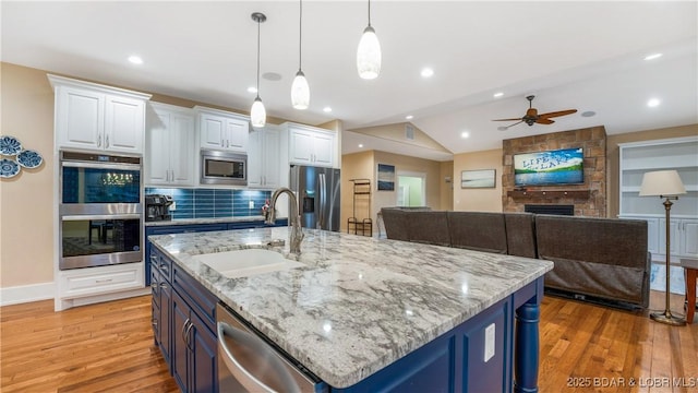 kitchen with light wood-type flooring, a sink, appliances with stainless steel finishes, and open floor plan