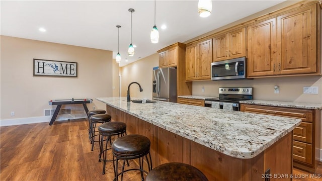 kitchen with a breakfast bar, an island with sink, a sink, dark wood finished floors, and stainless steel appliances