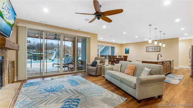 living room featuring ceiling fan, sink, light wood-type flooring, and a stone fireplace