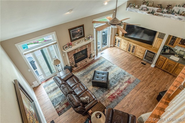 living room with sink, high vaulted ceiling, a brick fireplace, ceiling fan, and hardwood / wood-style floors