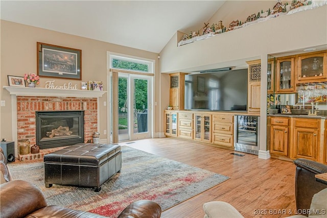 living room with wine cooler, bar, high vaulted ceiling, a brick fireplace, and light hardwood / wood-style flooring