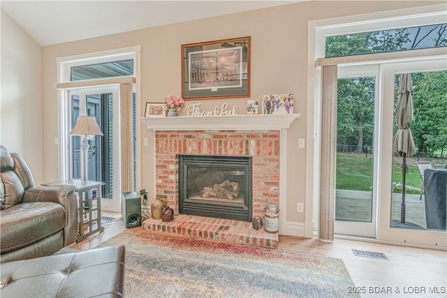 living room with lofted ceiling, hardwood / wood-style floors, and a brick fireplace