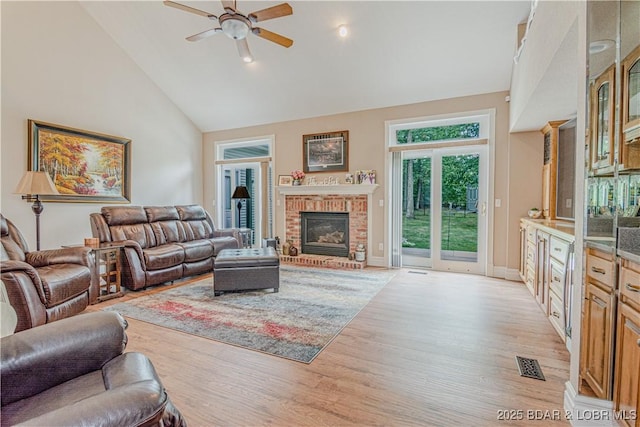 living room with ceiling fan, a brick fireplace, high vaulted ceiling, and light hardwood / wood-style flooring