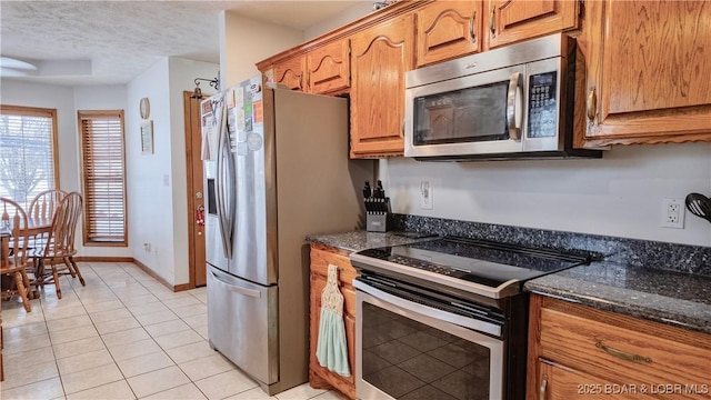 kitchen featuring light tile patterned floors, stainless steel appliances, dark stone counters, and a textured ceiling