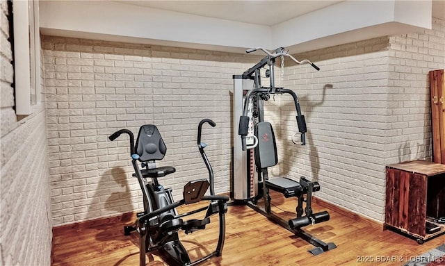 exercise area with light hardwood / wood-style flooring and brick wall