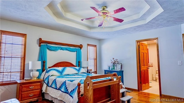 bedroom featuring baseboards, wood finished floors, a textured ceiling, ensuite bath, and a raised ceiling