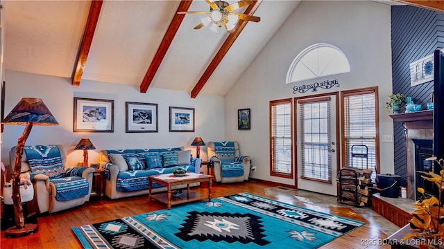 living room with wood-type flooring, high vaulted ceiling, beamed ceiling, ceiling fan, and a tiled fireplace