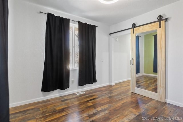 spare room with a barn door and dark wood-type flooring