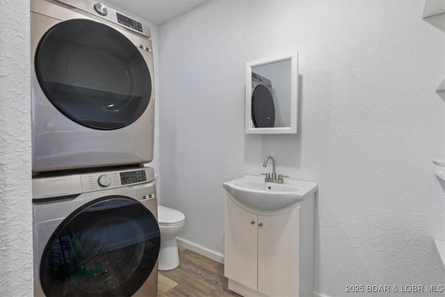 washroom with wood-type flooring, stacked washer and clothes dryer, and sink