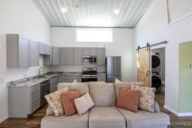 kitchen featuring gray cabinets, stainless steel appliances, stacked washer and clothes dryer, a high ceiling, and a barn door