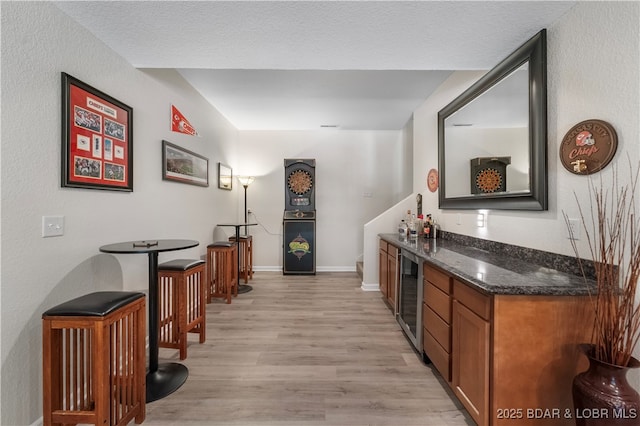 bar featuring dark stone countertops, beverage cooler, and light wood-type flooring