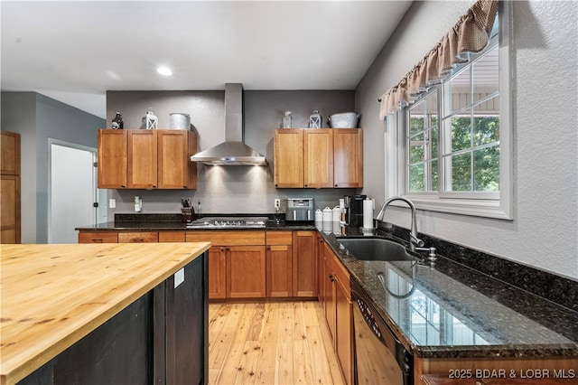 kitchen featuring sink, light hardwood / wood-style flooring, dark stone countertops, stainless steel appliances, and wall chimney exhaust hood