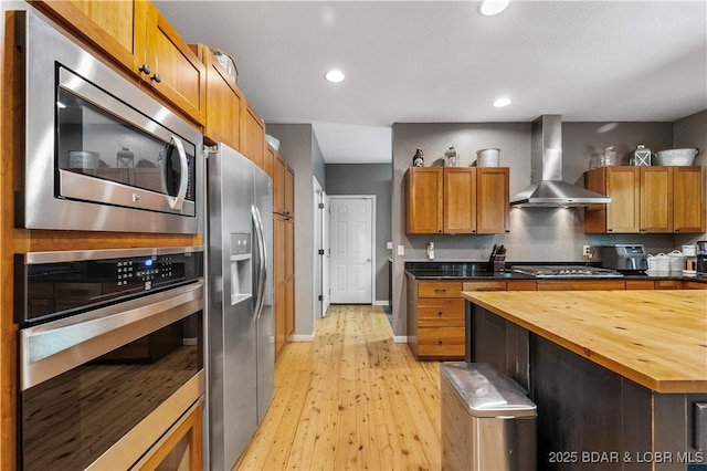 kitchen featuring stainless steel appliances, wooden counters, light hardwood / wood-style flooring, and wall chimney range hood