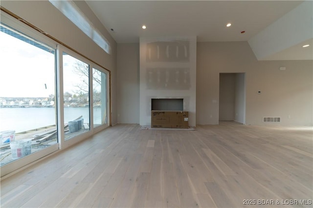 unfurnished living room with a water view, high vaulted ceiling, and light wood-type flooring