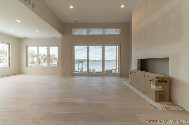 unfurnished living room with a water view, light hardwood / wood-style flooring, and a wealth of natural light