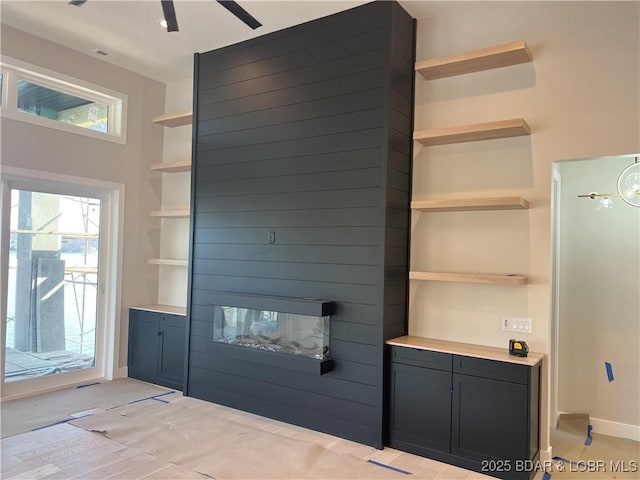 unfurnished living room with baseboards, visible vents, a multi sided fireplace, and built in shelves