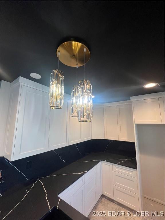 kitchen featuring pendant lighting, tasteful backsplash, dark countertops, white cabinets, and an inviting chandelier