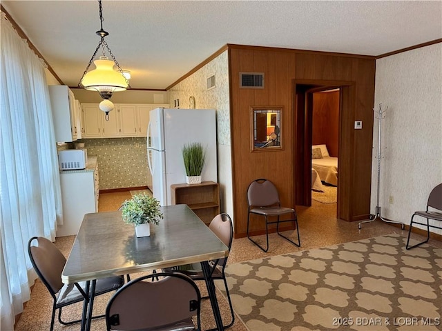 dining room featuring ornamental molding, wooden walls, and a textured ceiling