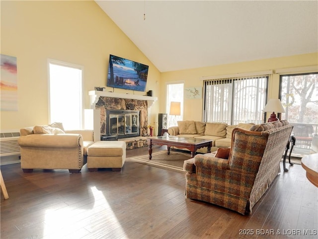 living area with high vaulted ceiling, a stone fireplace, and dark wood-type flooring