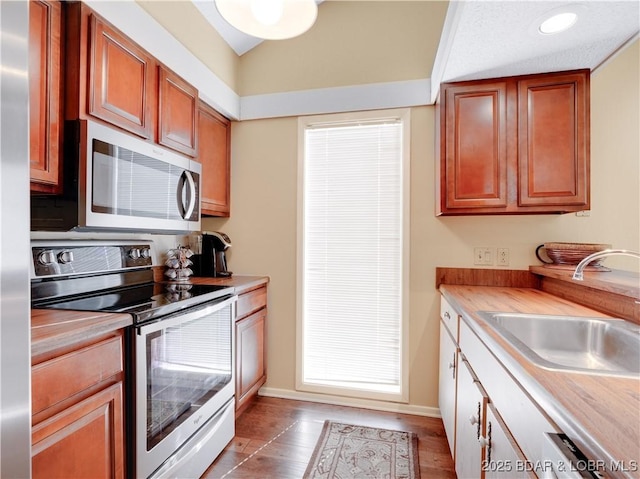 kitchen with stainless steel appliances, wood finished floors, a sink, and light countertops