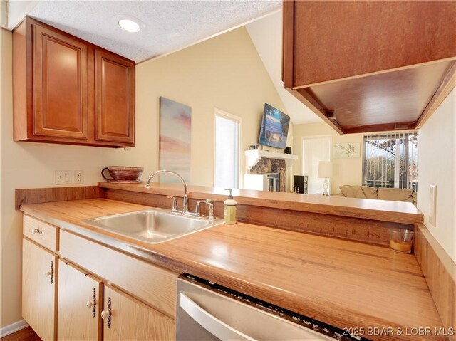 kitchen with vaulted ceiling, a stone fireplace, butcher block counters, sink, and a textured ceiling