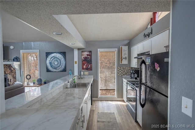 kitchen featuring sink, white cabinets, backsplash, stainless steel range with electric stovetop, and black fridge