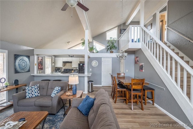 living room with beamed ceiling, ceiling fan with notable chandelier, high vaulted ceiling, and light hardwood / wood-style flooring