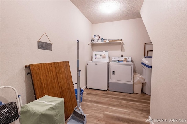 washroom with separate washer and dryer, light wood-type flooring, and a textured ceiling