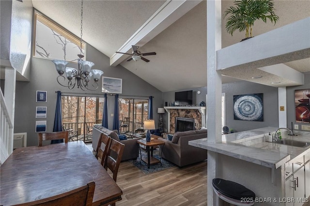 dining room featuring a stone fireplace, sink, high vaulted ceiling, a textured ceiling, and hardwood / wood-style floors