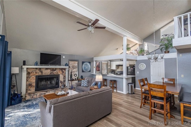 living room with a stone fireplace, high vaulted ceiling, light hardwood / wood-style flooring, beamed ceiling, and ceiling fan with notable chandelier