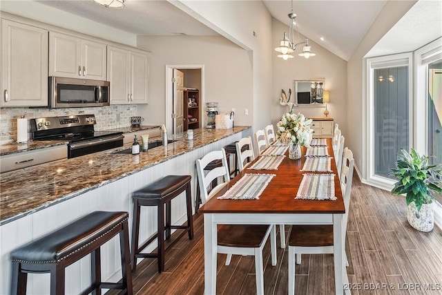 kitchen featuring appliances with stainless steel finishes, a kitchen bar, dark stone counters, and decorative light fixtures