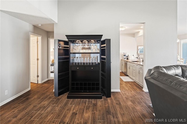 bar featuring dark wood-type flooring, light stone countertops, sink, and white cabinets