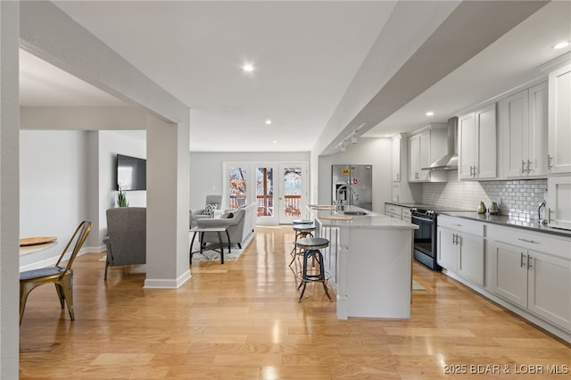 kitchen featuring a kitchen island with sink, stainless steel appliances, tasteful backsplash, a kitchen bar, and wall chimney exhaust hood