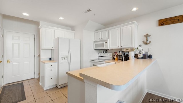 kitchen with white cabinetry, a kitchen bar, light tile patterned floors, kitchen peninsula, and white appliances