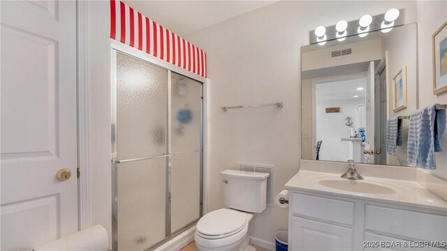 bathroom featuring a shower with door, vanity, and toilet