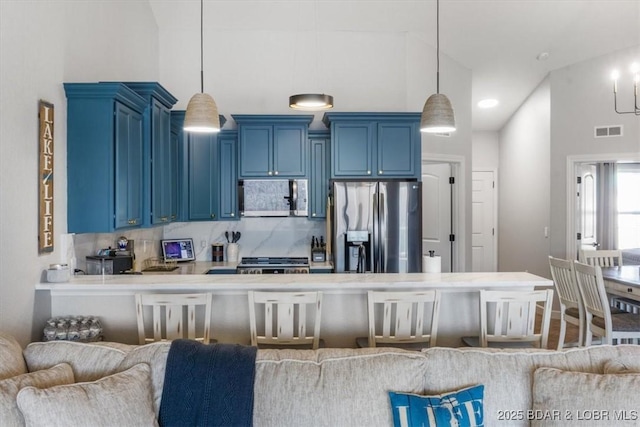 kitchen featuring appliances with stainless steel finishes, a breakfast bar area, backsplash, hanging light fixtures, and blue cabinetry