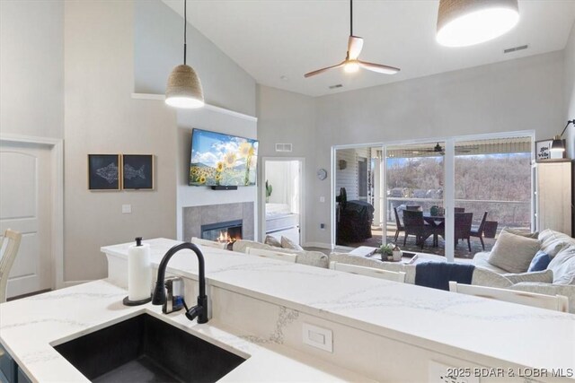 kitchen featuring pendant lighting, ceiling fan, a tiled fireplace, and sink