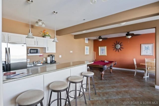 kitchen with a breakfast bar, white cabinetry, hanging light fixtures, stainless steel appliances, and beamed ceiling