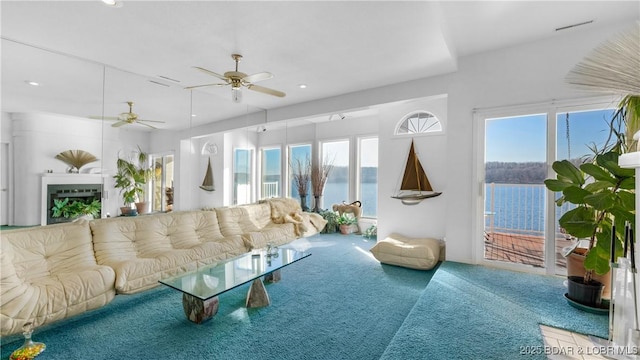 carpeted living room with ceiling fan and a water view