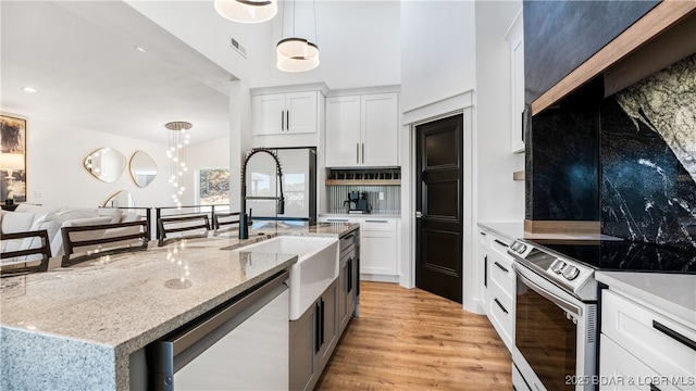 kitchen with appliances with stainless steel finishes, hanging light fixtures, light stone countertops, white cabinets, and a center island with sink