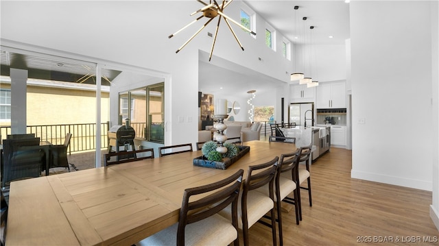 dining area with a high ceiling, a chandelier, and light wood-type flooring