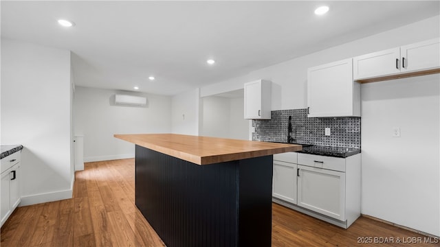 kitchen with butcher block countertops, tasteful backsplash, wood-type flooring, a wall unit AC, and white cabinets