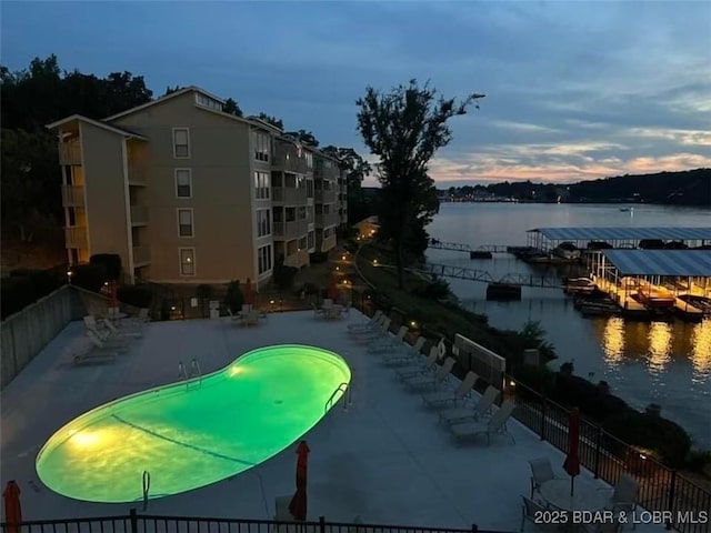 pool at dusk featuring a patio and a water view