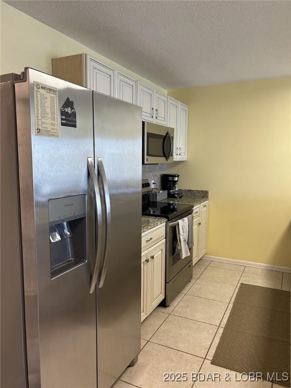 kitchen with light tile patterned flooring, dark stone countertops, white cabinets, stainless steel appliances, and a textured ceiling