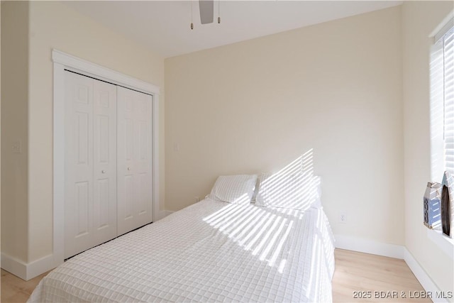 bedroom with light wood finished floors, a ceiling fan, baseboards, and a closet