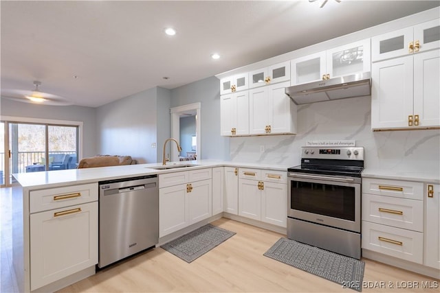 kitchen with a peninsula, stainless steel appliances, light countertops, under cabinet range hood, and a sink