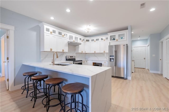 kitchen featuring backsplash, appliances with stainless steel finishes, a sink, light stone countertops, and a peninsula