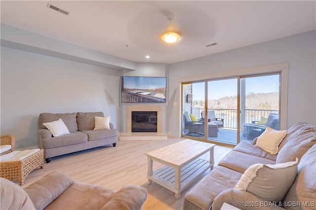 living area with a glass covered fireplace, visible vents, light wood-style flooring, and recessed lighting