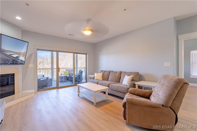 living room with light wood-type flooring, ceiling fan, a premium fireplace, and recessed lighting