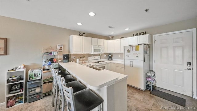 kitchen with white appliances, a breakfast bar, kitchen peninsula, and white cabinets